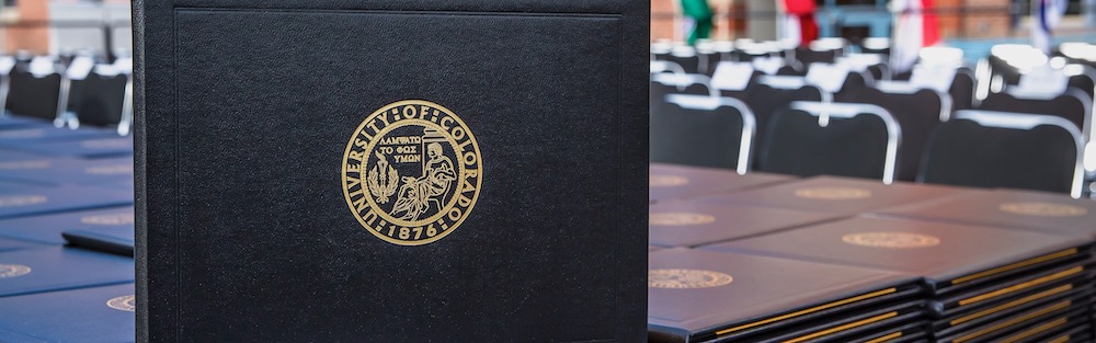 A sleeve for a CU Denver diploma stands on top of many other sleeves for diplomas.