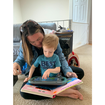 Young child sit's with SLP, using his AAC device to engage in book-reading.