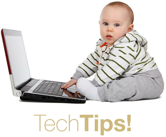 Baby sits at a laptop with hand on keyboard, looking at viewer.