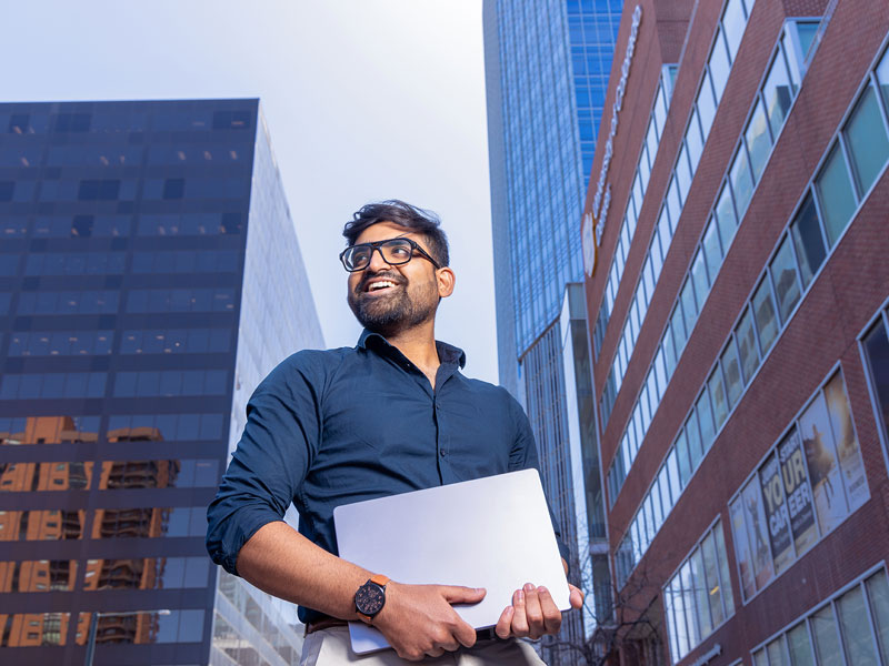 CU Denver student holding laptop standing outside of CU Denver building in downtown Denver