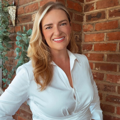 Leigh Pinner wearing white blouse in front of brick wall