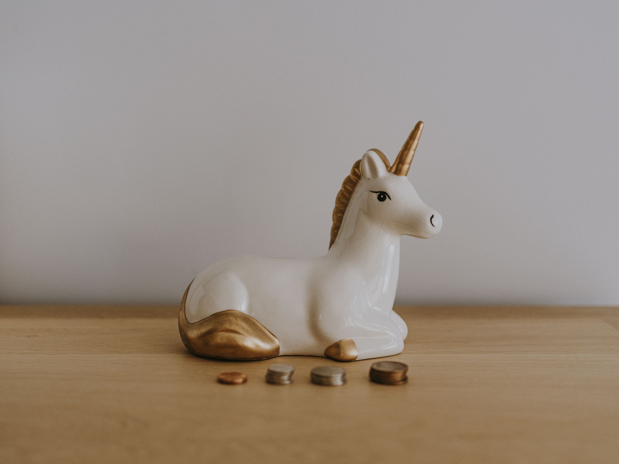 Pigg bank glass unicorn with coins next to it sitting on a desk