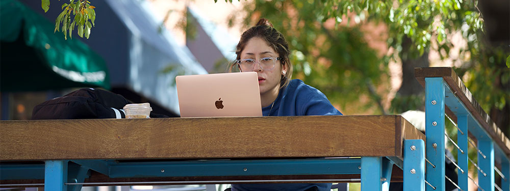 CU Denver student writing outside on their laptop