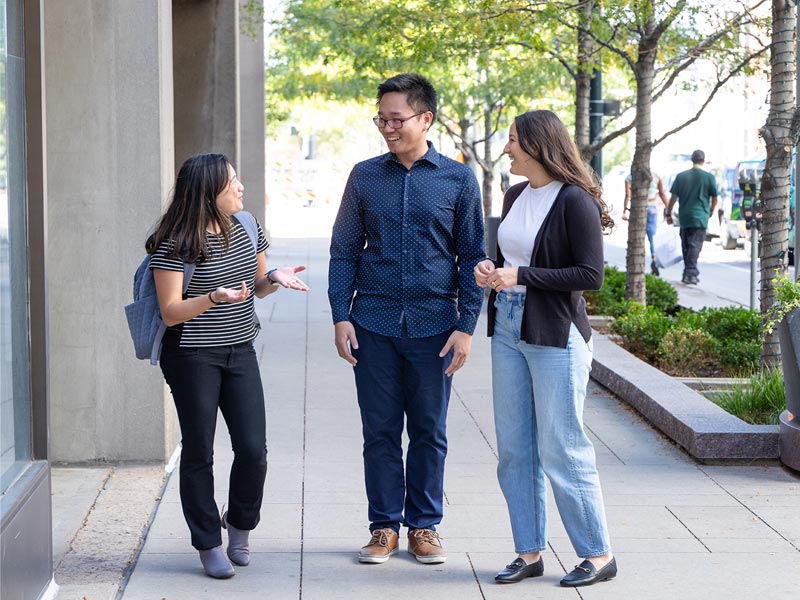 Three CU Denver students talking while standing outside of building on sidewalk