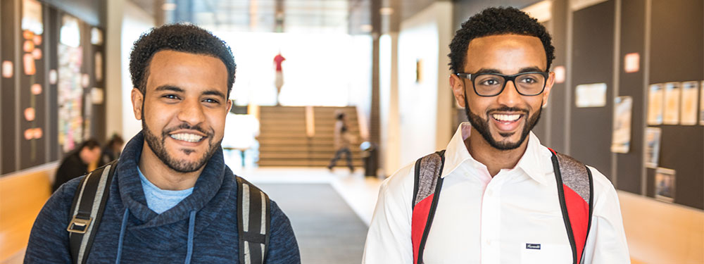Two CU Denver students walking smiling in campus halls