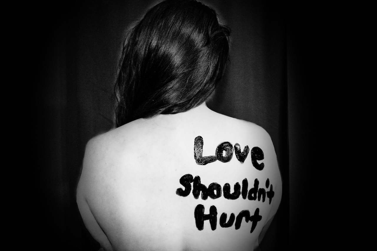 Love shouldn't hurt written on someones back in black paint