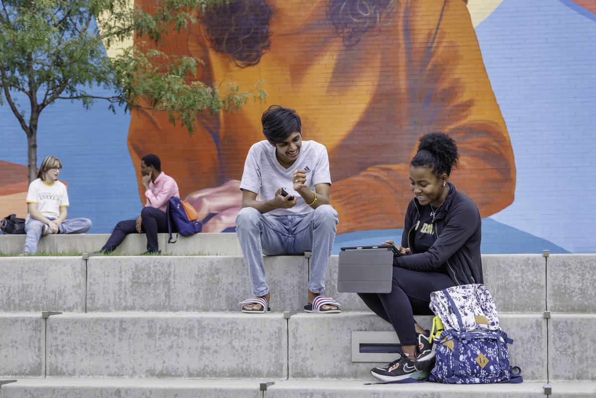 CU Denver students sitting outside of the Student Commons Building mural