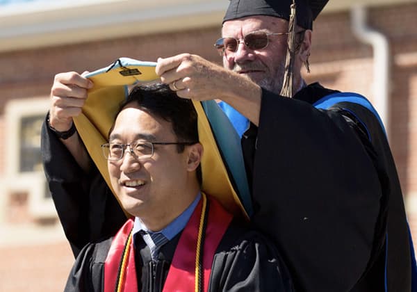 A doctoral graduate receives his hood at commencement