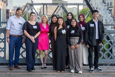 Chancellor Michelle Marks smiles with a group of CU Denver scholarship students on a bridge outside with the city in the background.