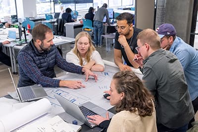 Six people gathered around a table with blueprints working together.