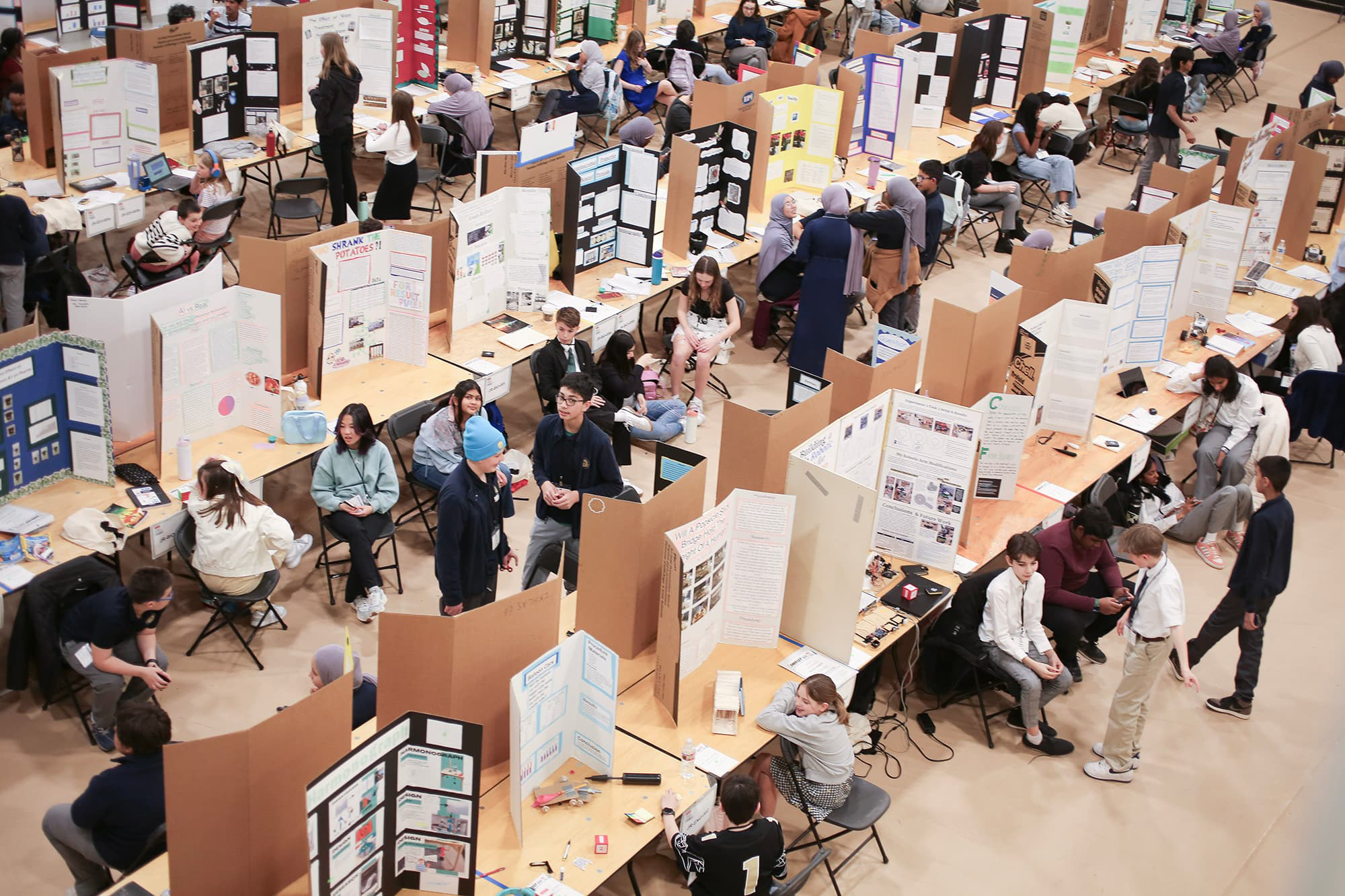 Above view of the CoorsTek Denver Metro Regional Science and Engineering Fair with rows of tables and posters with students. 