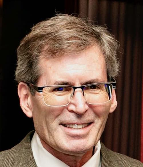Bob Wolfson in a tan suit, square glasses, brown with salt and pepper hair, and smiling with his teeth.