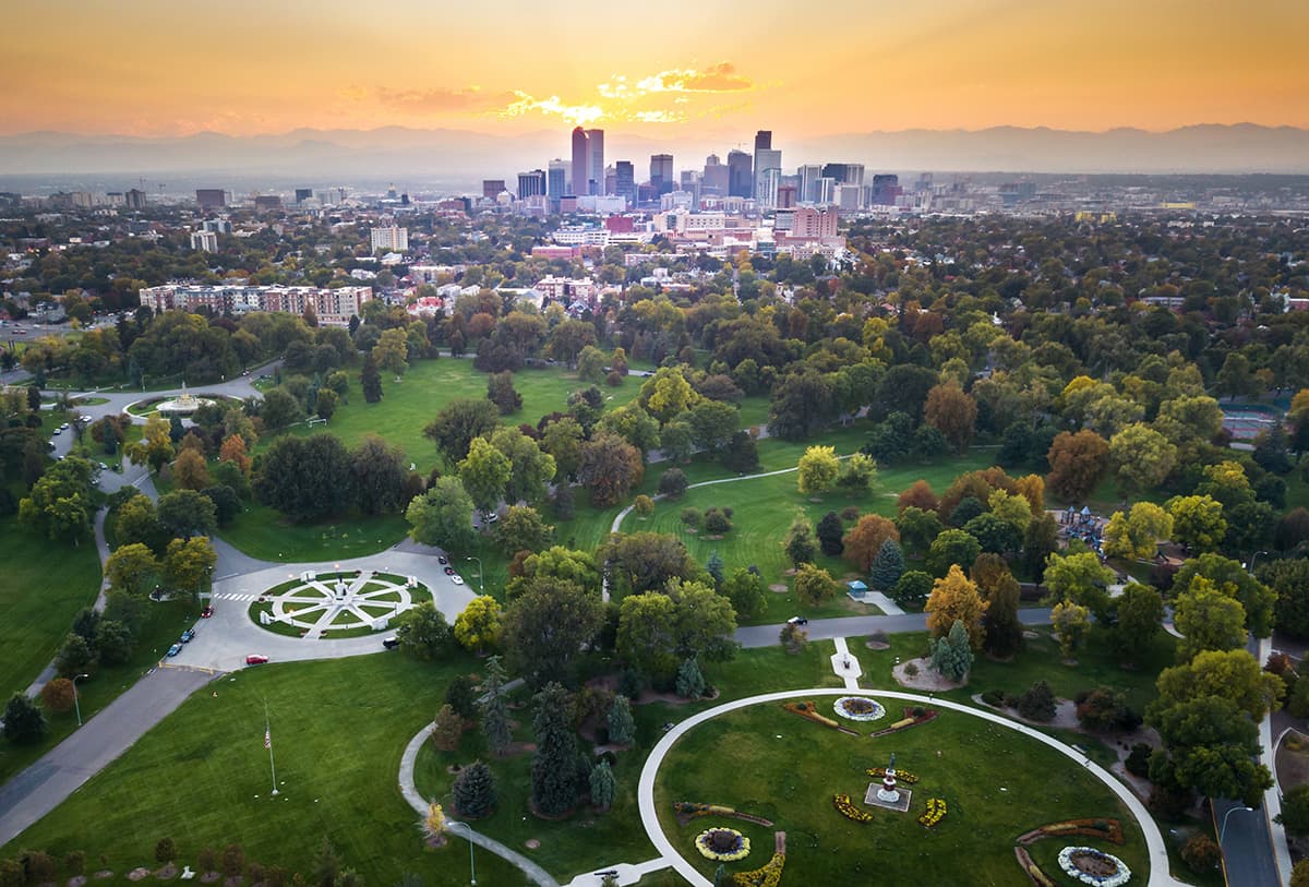 Aerial view of Denver skyline with a large green park in the foreground and a gold sky in the distance.  .
