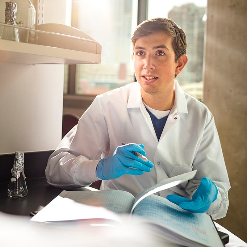 Man in a white coat and blue latex gloves thumbing through papers talking with someone and smiling.