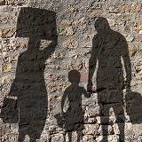 Silhouettes of two adults and a young child appearing to be traveling cast onto a gray textured wall.