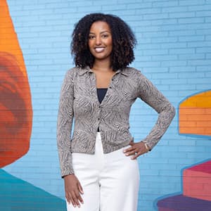 Woman in business professional attire stands in front of a colorful wall smiling with her teeth.