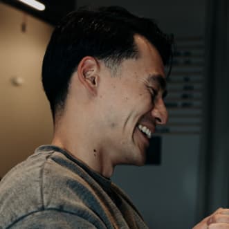 Profile of a man with dark hair, smiling with his teeth.