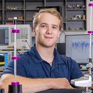 Man in a blue collard shirt and a closed-mouth smile sits in a lab.