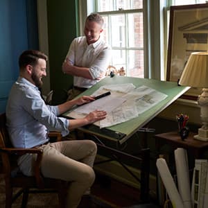 Two men at an architect drafting table talking and smiling.