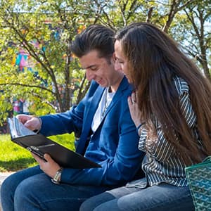 Two people seated outside looking at a CU Denver branded binder together.