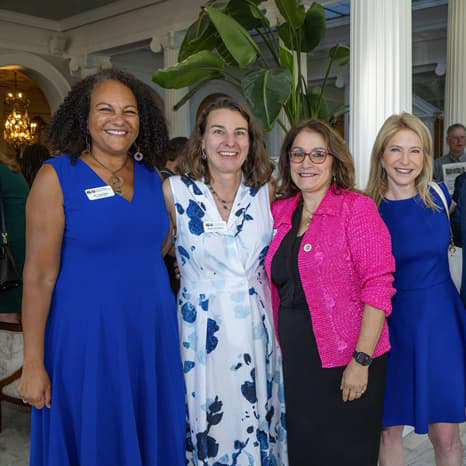 Lisa Roy, Katy Anthes, Susana Cordova, and Michelle Marks standing arm-in-arm, all smiling with their teeth.