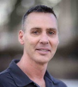 Headshot of a man in a blue polo and short dark hair with a soft smile that shows his teeth.