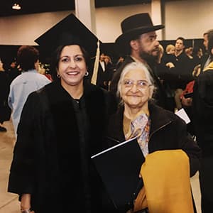 Woman in commencement regalia smiles with another woman.