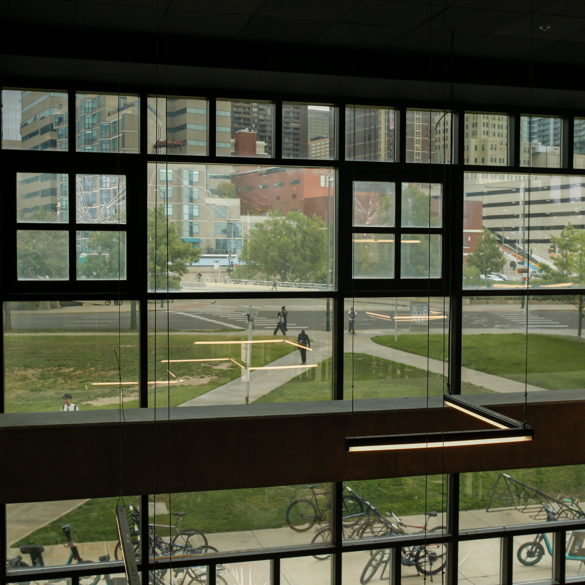 A view from inside of North Classroom Building of campus with people walking and bicycles parked outside.