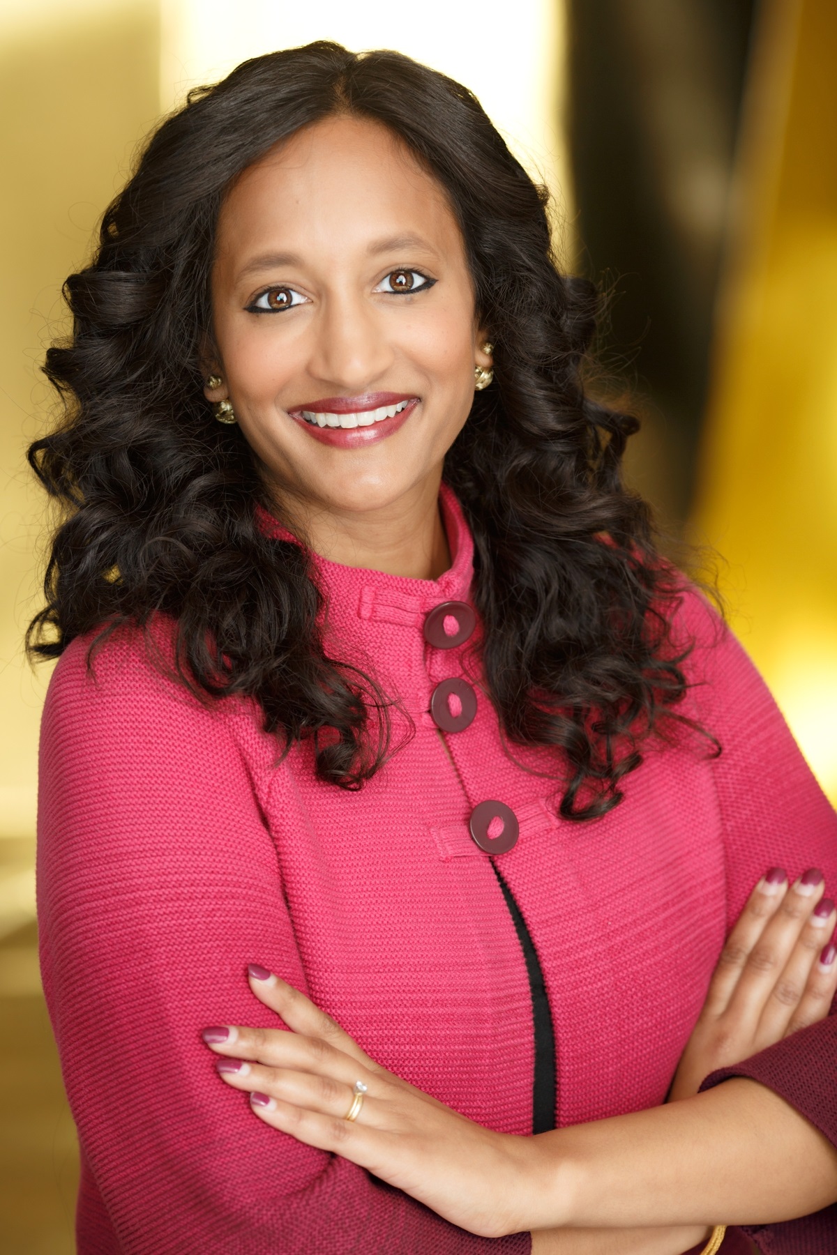 Woman with dark hair wearing a pink jacket facing the camera and smiling
