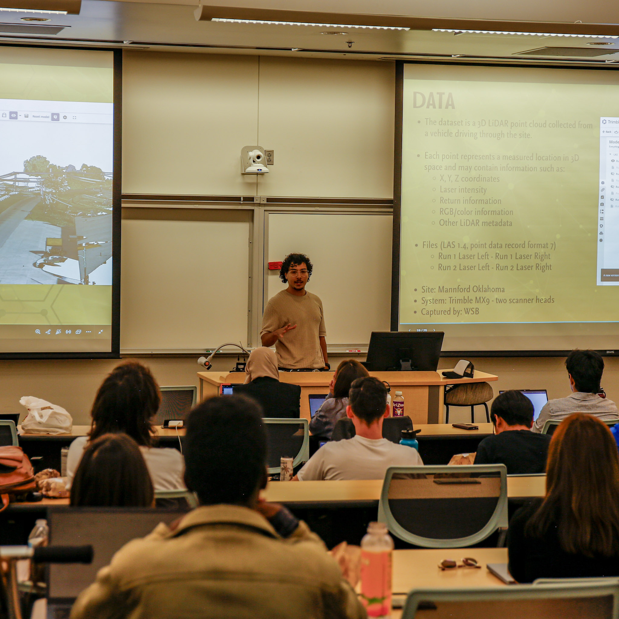 A presenter stands at the front of a classroom as attendees watch a presentation about LiDAR data during the AI4Infrastructure challenge kickoff.