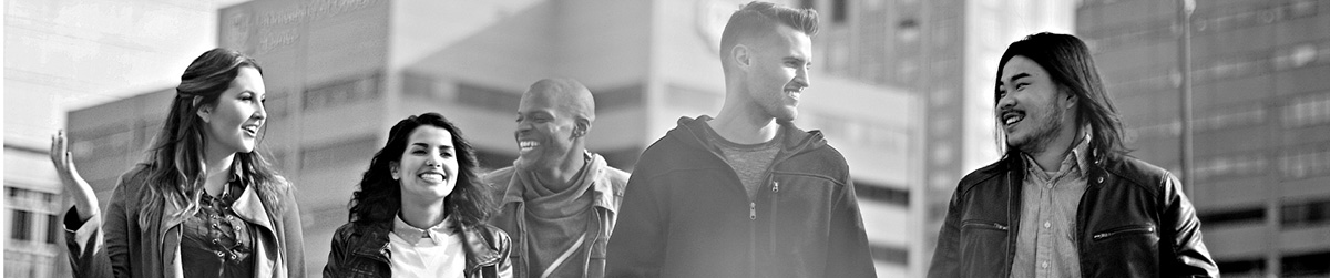 A group of five students walking together outdoors in an urban setting, with tall buildings in the background. They appear to be engaged in conversation, dressed casually, and moving in the same direction.
