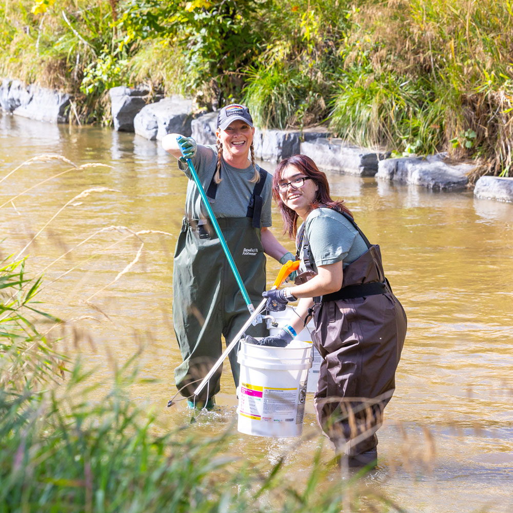 Two people cleaning trash out of river