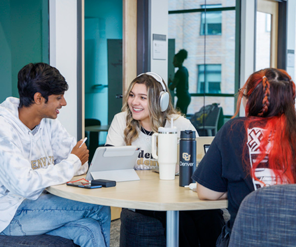 Three CU Denver students engaging in conversation while sitting at table in shared study space