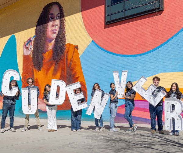 Students holding CU Denver lighted letters in front of mural on campus
