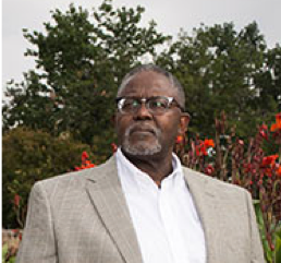 Headshot of Benjamin Moultrie in business suit outdoors with flowers behind him
