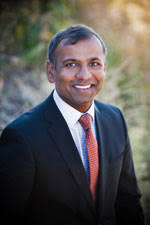 headshot of Venu outdoors smiling in business suit and tie