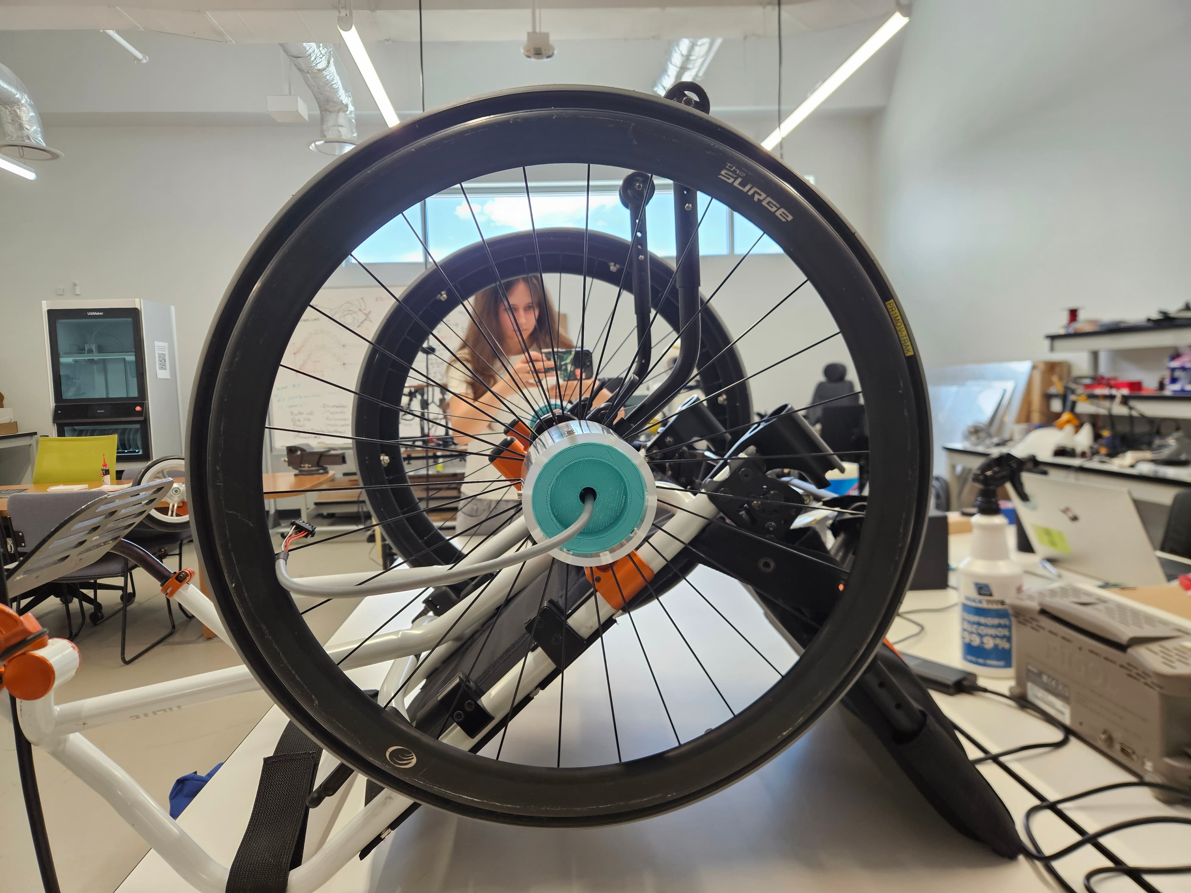 Researcher examines the SPIN sensor device mounted on a manual wheelchair wheel in a laboratory setting.