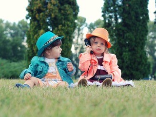 Two little girls sitting in the grass using phone together.