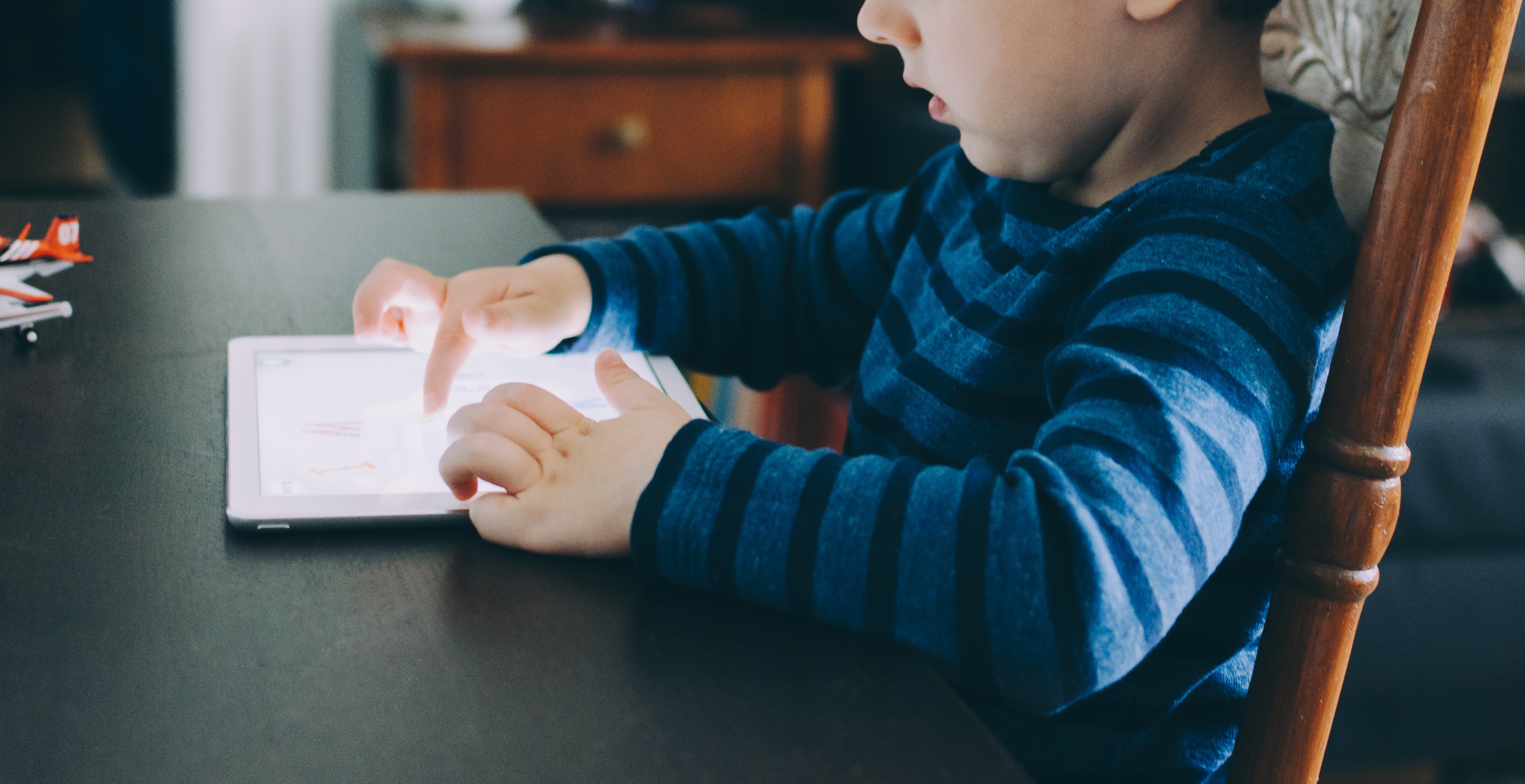 A child sitting at a table and using a tablet
