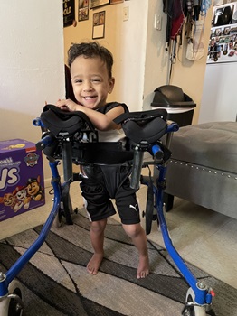 Young boy using gait trainer to stand, smiling