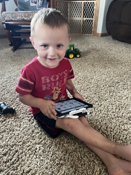 Young boy using AT device with Proloquo2Go app, smiling