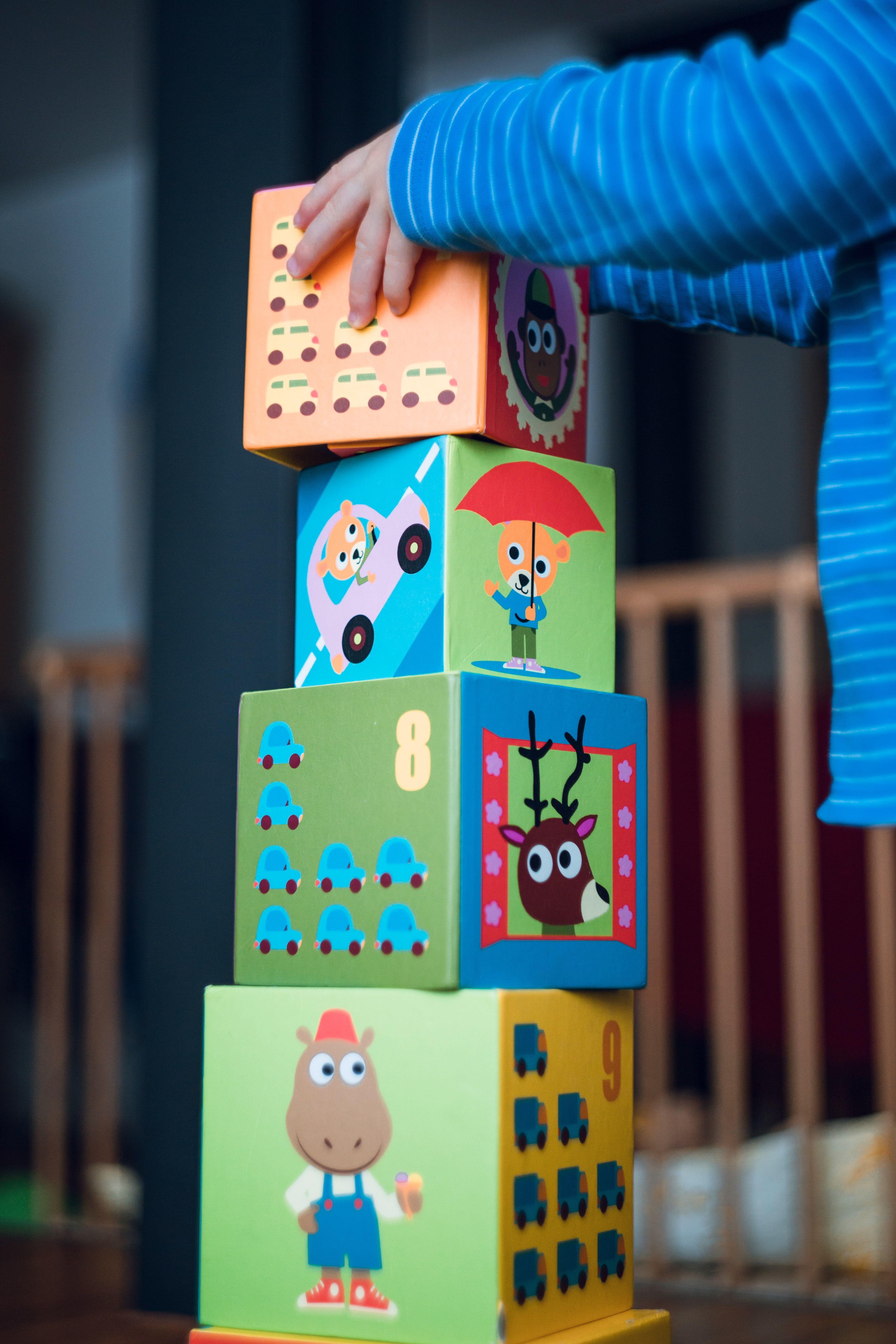 Small child stacks fourth block in tower of blocks.
