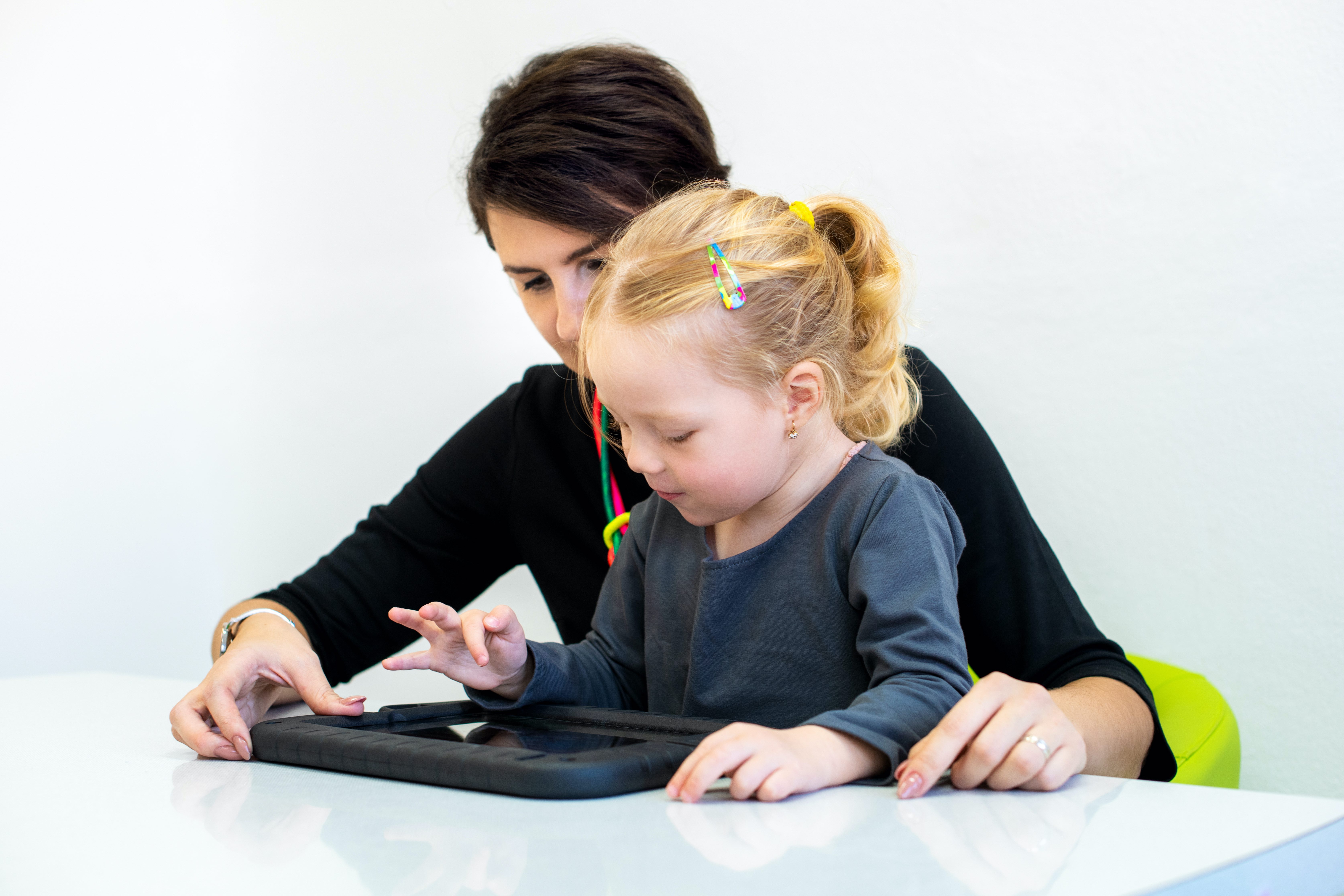 Therapist sitting with little girl, using a tablet together.