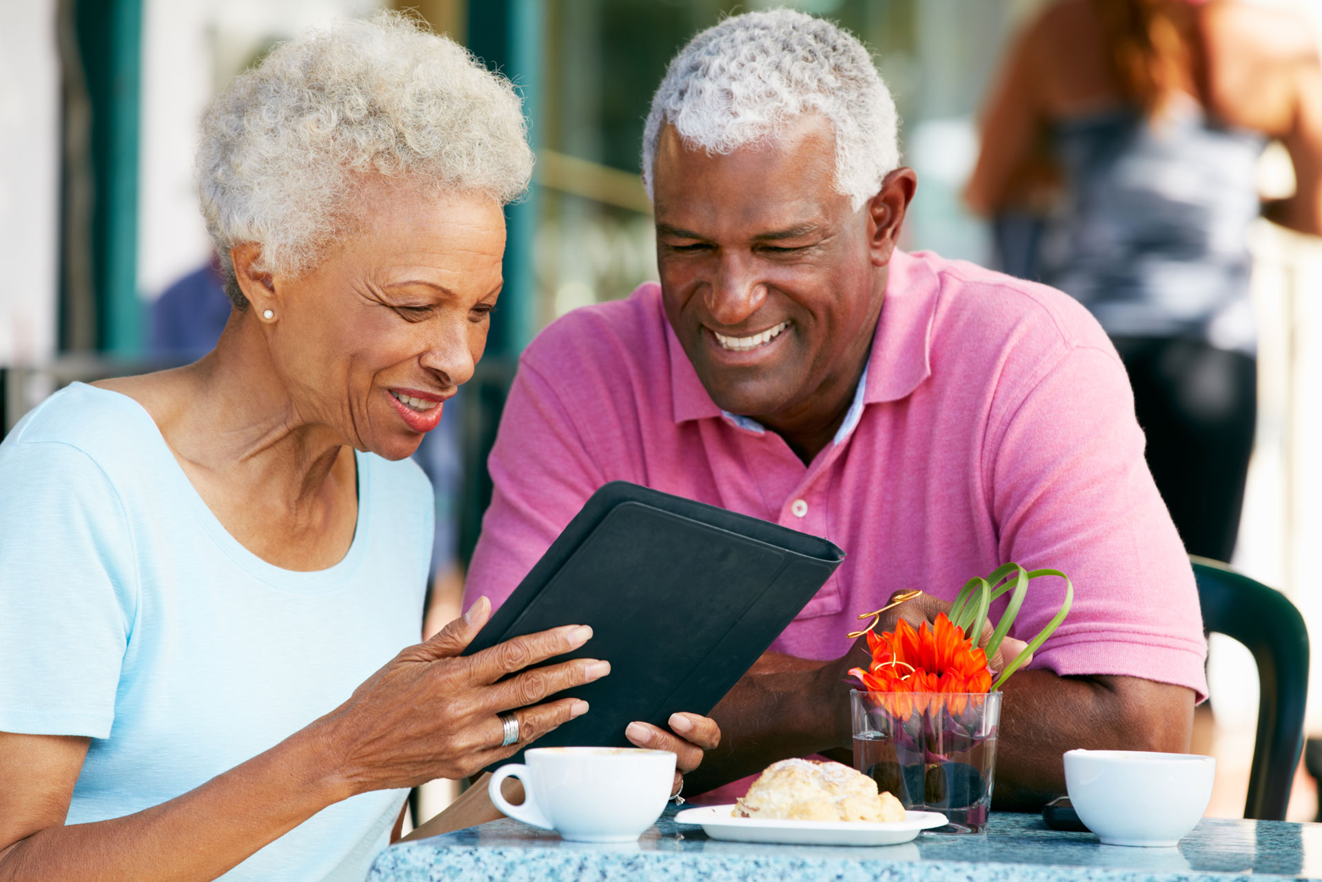 Smiling older couple uses tablet outdoors