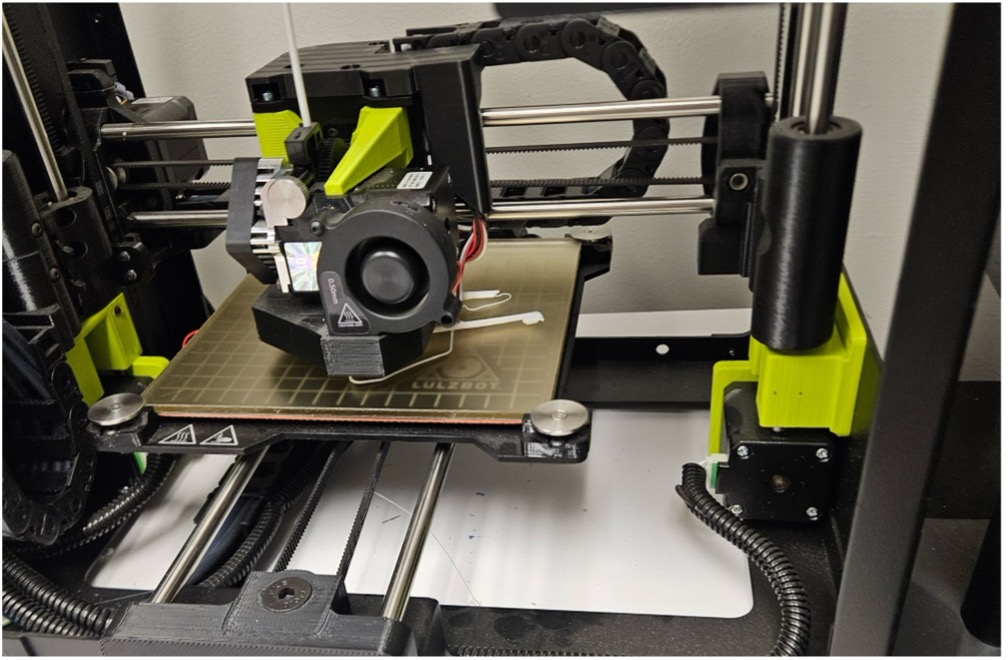 A 3D printer with bright green parts, its print head positioned over the build plate.