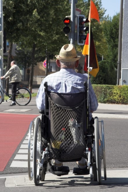 elderly man sitting in his wheelchair at a crosswalk 