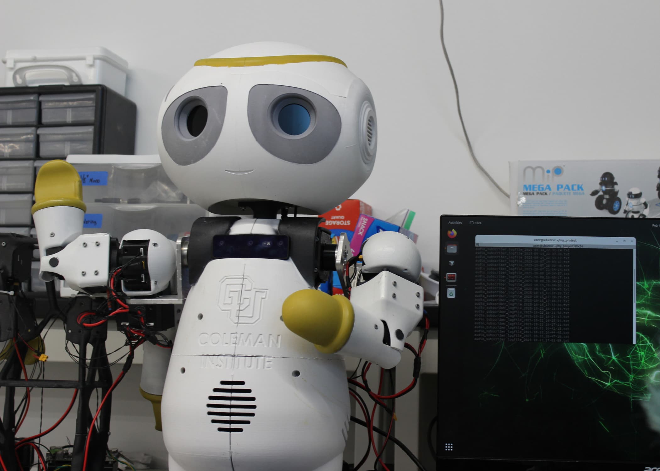A small friendly robot sits on a lab table. C U Coleman Institute Logo on it's chest.