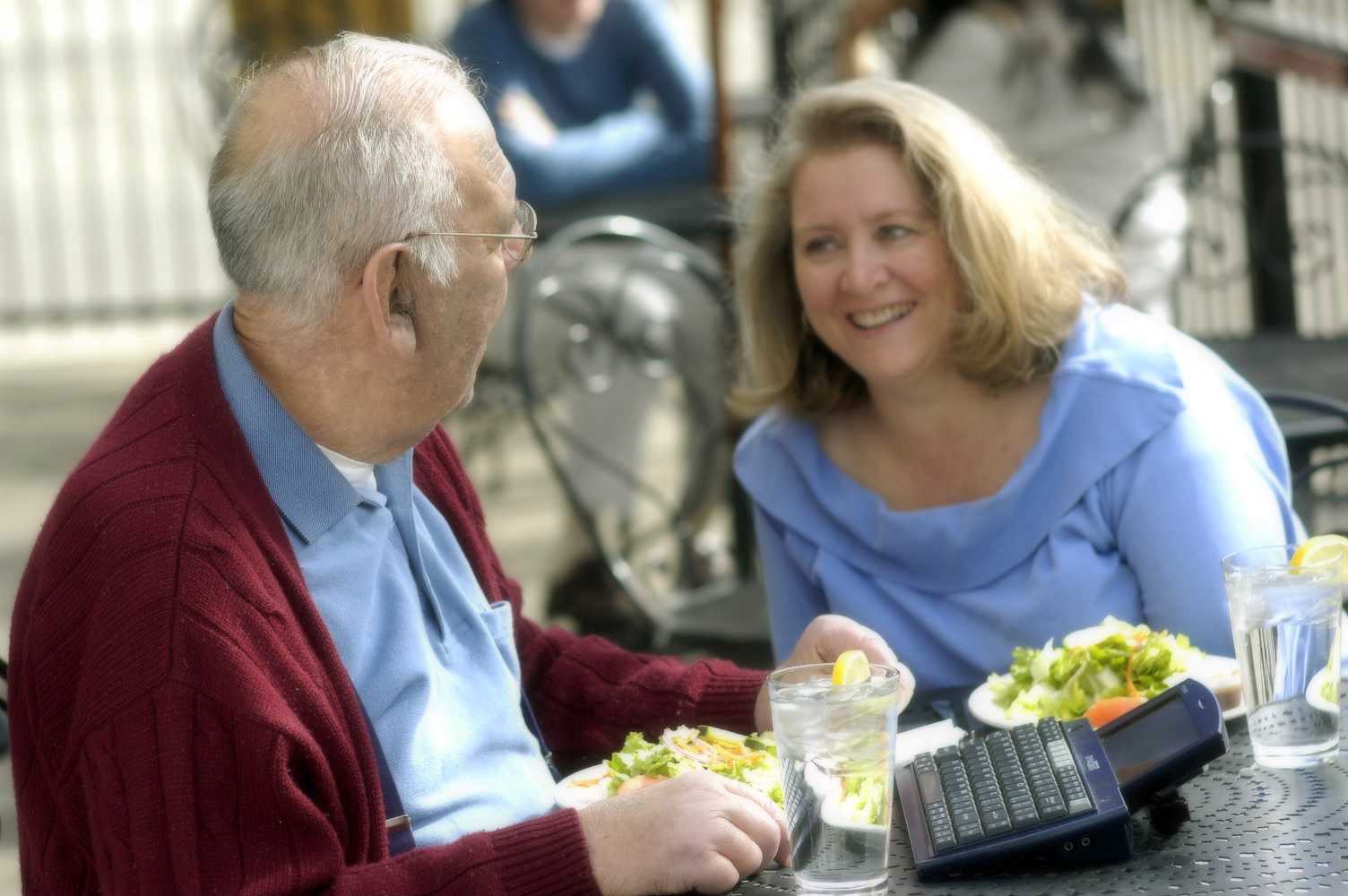 Two people enjoy a conversation at an outdoor cafe. One of them is using a communication device.