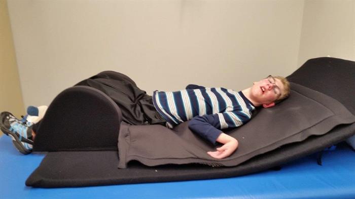 a young man with cerebral palsy lies with his legs supported on a certified sleep system mattress