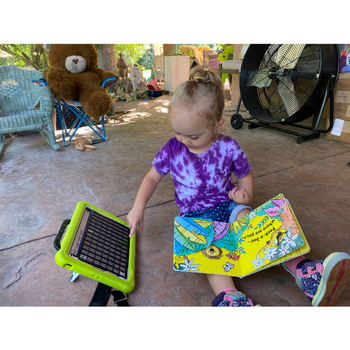via pro a child reaching for an aac device while holding an open book in her lap